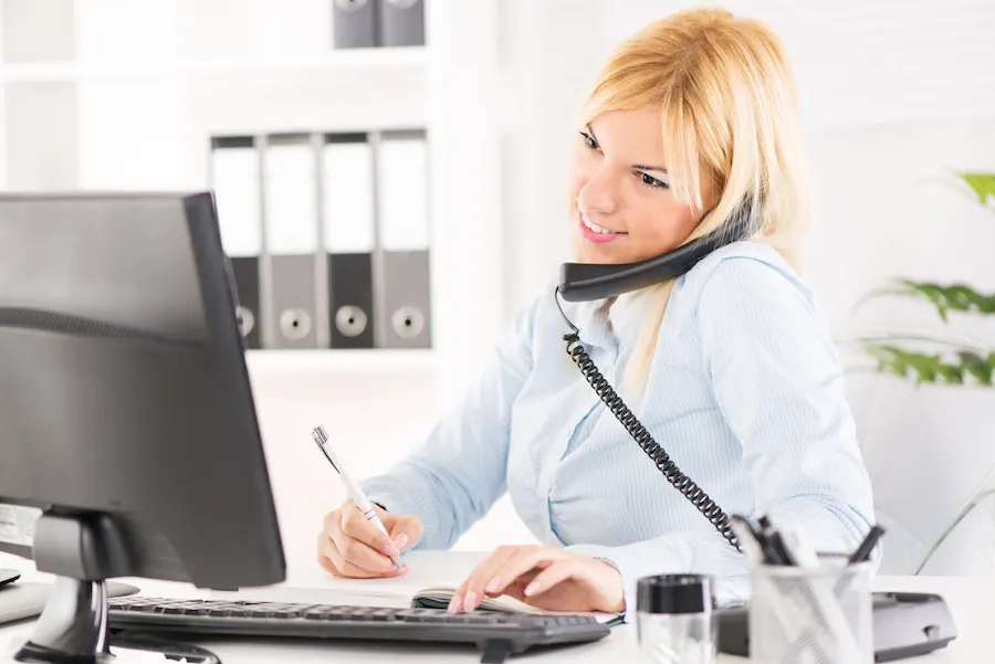 A smiling receptionist taking a phone enquiry at her desk